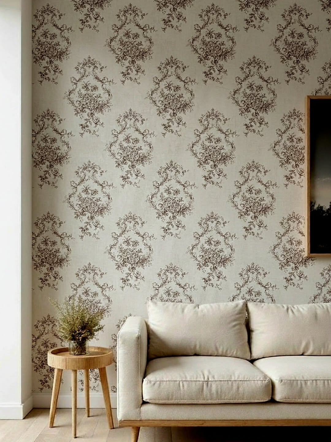 A living room interior featuring a wall covered in cream wallpaper with a repeating brown vintage floral pattern. In front of the wall sits a modern c
